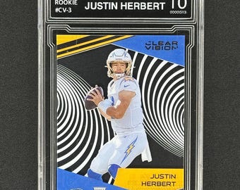 May include: A graded Justin Herbert rookie trading card from the 2020 Chronicles series. The card is a Gem Mint 10 and features a black and white swirl design with a blue and yellow border. The card has a clear vision logo and a rookie card logo.