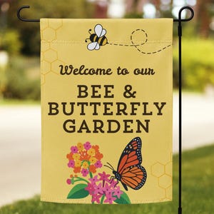 May include: A yellow garden flag with the text "Welcome to our BEE & BUTTERFLY GARDEN". The flag features a bee, a butterfly, and colorful flowers. The flag is hanging on a black metal stand in a grassy yard.