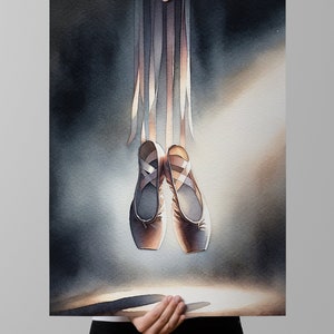 A woman holding up a high quality watercolor print in a white frame, showing a pair of Ballet Pointe Dancing Shoes.