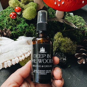 May include: A small brown glass bottle with a black spray nozzle and label that reads "Deep in the Woods Breathe & Ground Sage, Rosemary, Balsam Fir, Cedarwood, Hematite & Emerald"