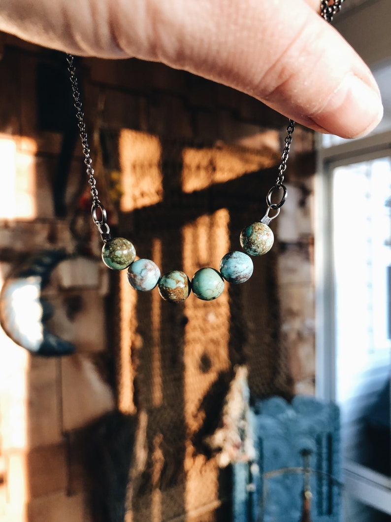 May include: A turquoise and green stone necklace with a silver chain. The necklace has seven stones, each with a different pattern.