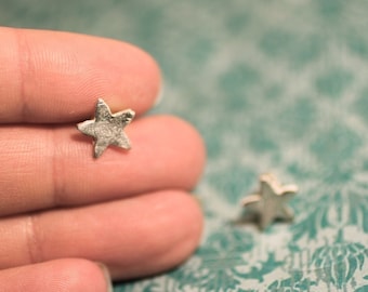 May include: A pair of silver star-shaped earrings. The earrings are small and delicate, and they have a textured surface.