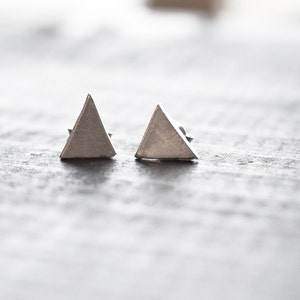 May include: A pair of silver triangle stud earrings. The earrings are simple and modern in design.
