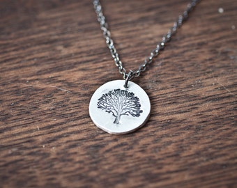 Puede incluir: Un collar de plata con un colgante redondo que presenta un diseño de árbol detallado.