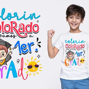 Puede incluir: Camiseta blanca con texto y gráficos coloridos. La camiseta presenta las palabras "colorin Colorado nos vamos a 1er Grad" en una fuente lúdica, junto con un graduado de dibujos animados y un sol con gafas de sol. Una persona lleva la camiseta.