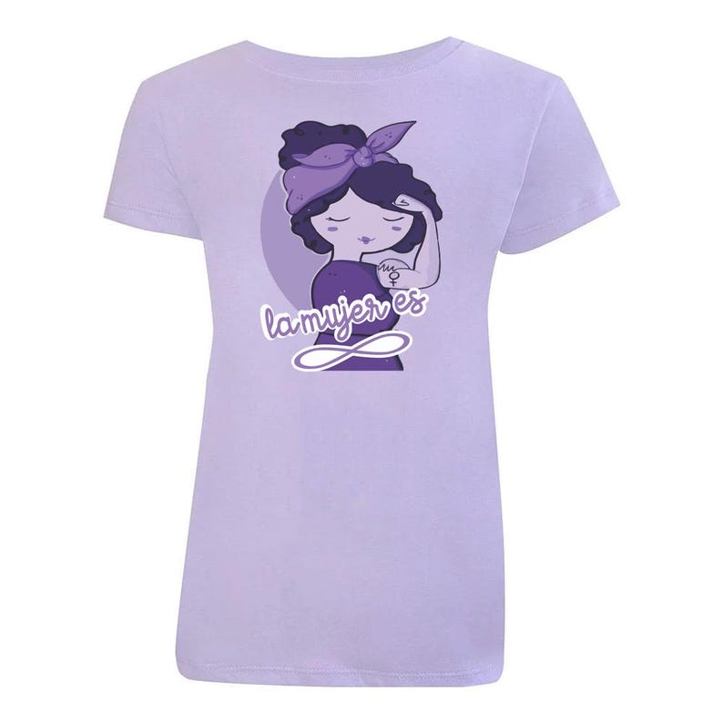 K&ouml;nnte beinhalten: Lilafarbenes T-Shirt mit einer Cartoon-Illustration einer Frau, die die Faust in die Luft reckt. Die Frau tr&auml;gt ein lilafarbenes Stirnband und hat ein lilafarbenes Tattoo auf dem Arm. Der Text "la mujer es" ist unter der Frau in lilafarbener Schrift geschrieben.