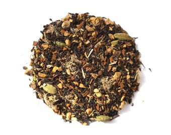 May include: A top-down view of a pile of chai tea blend. The blend includes dark tea leaves, light brown cinnamon sticks, beige ginger pieces, and green cardamom pods. The tea is scattered on a white background.