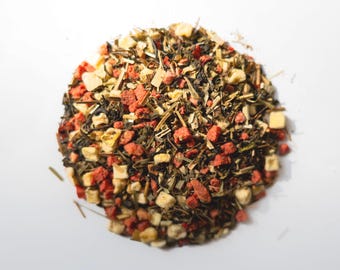 May include: A close-up shot of a pile of loose leaf tea. The tea blend features a mix of green tea leaves, dried red berries, and small, light-colored fruit pieces. The tea is arranged on a white surface.