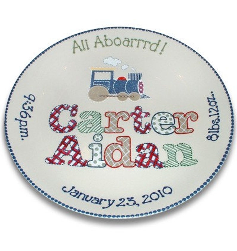 May include: A white ceramic plate with blue trim and a train design. The plate is personalized with the names "Carter Aidan", the date "January 23, 2010", the time "6:56pm", and the weight "8lbs 12oz".