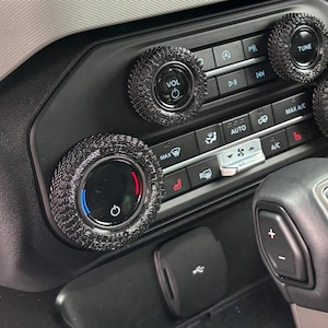 May include: Close-up of a car's dashboard with black and silver knobs. The knobs have a tire tread pattern and are labeled "VOL", "TUNE", and "DUAL".