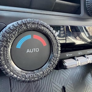 May include: Black car interior with custom air vent covers. The covers are designed to look like tires and are placed around the air vents and control knobs. The control knob has a blue to red temperature gauge and the word "AUTO".