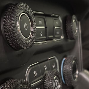 May include: Close-up of a car's dashboard with several black knobs with a textured surface. The knobs have silver rings around them and some have text on them, including "AUTO" and "ON/OFF".
