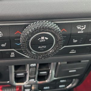 May include: Close-up of a car's dashboard with a black and gray interior. The dashboard features a row of buttons and knobs, including a knob labeled "AUTO" and another labeled "OFF".
