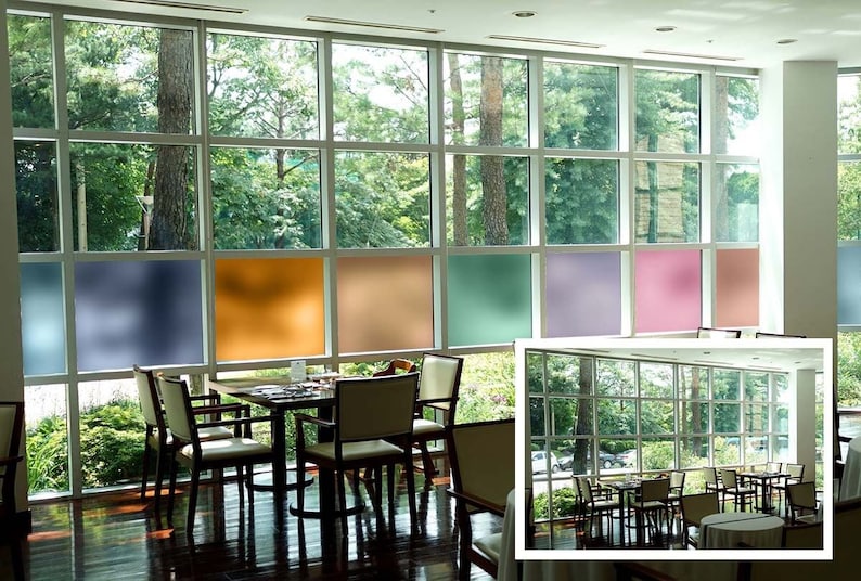 May include: A dining area with a large window featuring frosted glass panels in various colors, including blue, yellow, brown, green, purple, and pink. The window overlooks a lush green landscape. A table with four chairs is positioned in front of the window. Another dining area with a similar window and table and chairs is visible in the background.