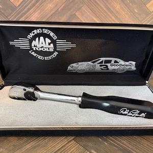 May include: A Mac Tools Racing Series limited edition ratchet with a chrome head and a black handle featuring a white signature. The tool is housed in a black presentation case with a white interior, displaying a graphic of a number 3 race car.