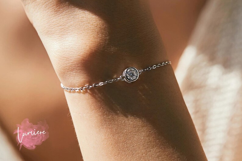 May include: A delicate silver chain bracelet with a single round clear crystal stone.