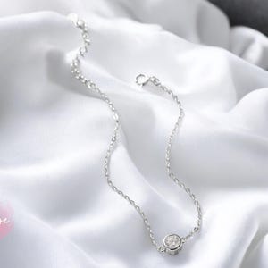 May include: A delicate silver chain bracelet with a single, clear cubic zirconia stone.