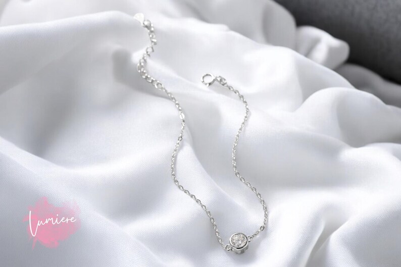 May include: A delicate silver chain bracelet with a single, clear cubic zirconia stone.