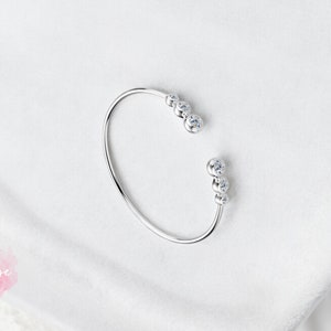 May include: A silver bangle bracelet with a row of five clear cubic zirconia stones on each side.