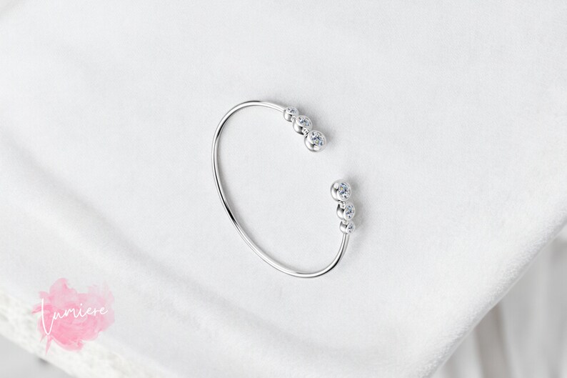 May include: A silver bangle bracelet with a row of five clear cubic zirconia stones on each side.