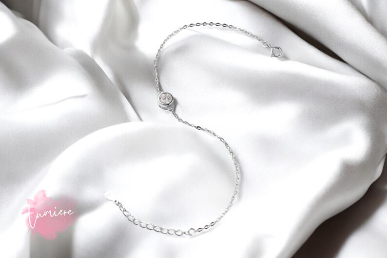 May include: A delicate silver chain bracelet with a single round clear crystal.