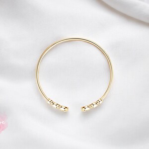 May include: A gold bangle bracelet with a simple design featuring small round beads at the ends.