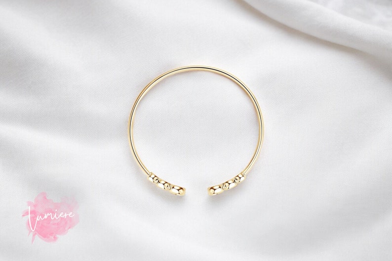 May include: A gold bangle bracelet with a simple design featuring small round beads at the ends.