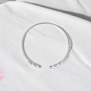 May include: A silver bangle bracelet with small round beads on each end.