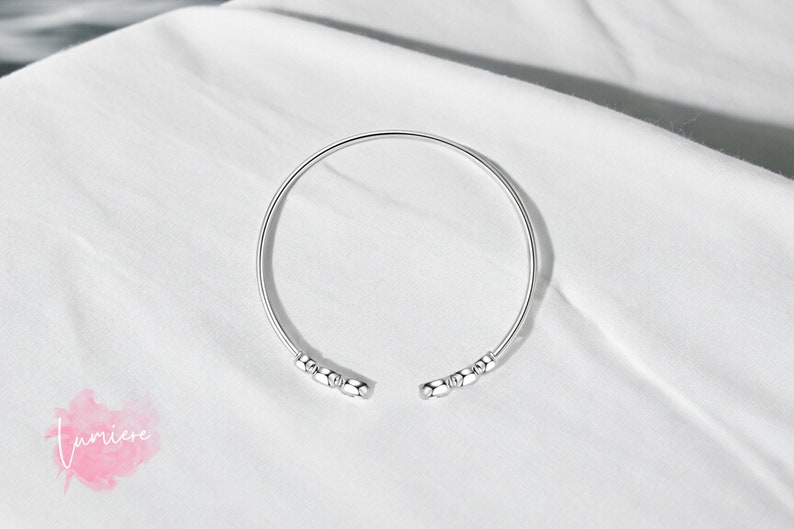 May include: A silver bangle bracelet with small round beads on each end.