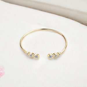 May include: A gold bangle bracelet with a row of clear cubic zirconia stones on each side.