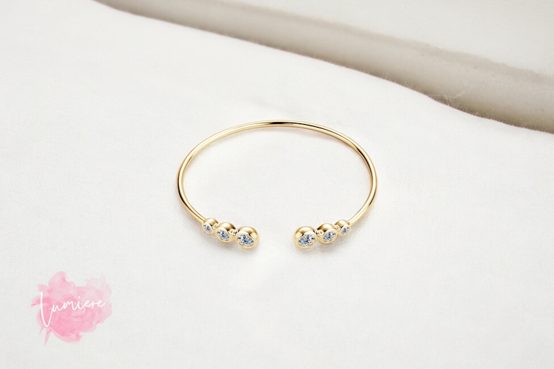 May include: A gold bangle bracelet with a row of clear cubic zirconia stones on each side.