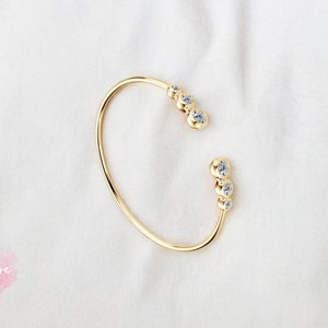 May include: A gold bangle bracelet with a cluster of small clear stones on each side.