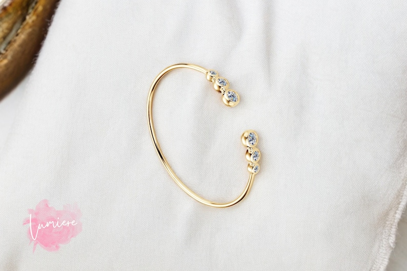 May include: A gold bangle bracelet with a cluster of small clear stones on each side.
