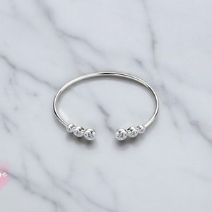 May include: A silver bangle bracelet with a row of clear cubic zirconia stones on each side.