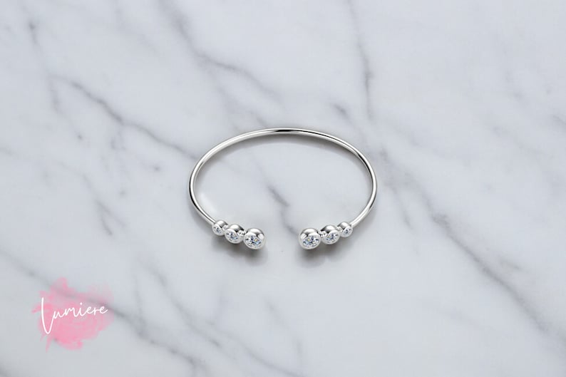 May include: A silver bangle bracelet with a row of clear cubic zirconia stones on each side.
