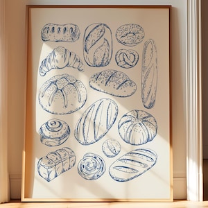 May include: A framed print featuring a collection of various bread illustrations in blue ink on an off-white background. The artwork includes depictions of croissants, baguettes, and other baked goods. The frame is a warm, natural wood tone, adding a touch of rustic charm.