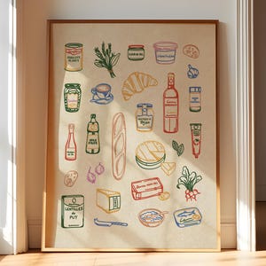 May include: A framed print featuring colorful illustrations of French food items. The artwork includes a croissant, wine bottle, cheese, baguette, and various canned goods. The illustrations are outlined in black with pops of red, green, and blue on a beige background.