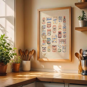 May include: A framed print featuring colorful illustrations of various food products, including crackers, peanut butter, and coffee. The artwork is displayed in a kitchen setting, alongside potted plants, wooden spoons, and a coffee maker. The print has a wooden frame.