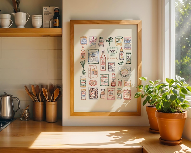 May include: A framed print featuring colorful illustrations of various Asian food ingredients. The artwork includes images of sauces, spices, and packaged goods, all with handwritten labels. The print is displayed on a wooden countertop near potted plants.