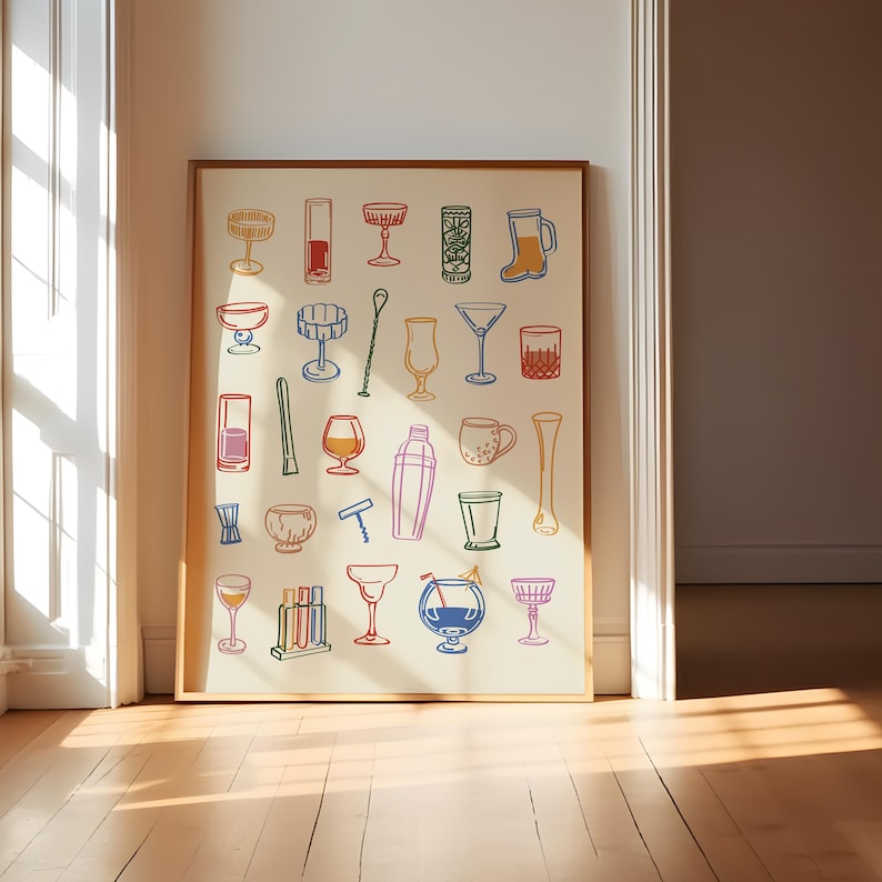 Op de afbeelding: Een ingelijste print met kleurrijke illustraties van verschillende cocktailglazen en bartools. Het kunstwerk bevat een cocktailshaker, martiniglazen en een kurkentrekker, allemaal omlijnd in verschillende kleuren tegen een cr&egrave;mekleurige achtergrond. De print wordt tentoongesteld in een kamer met een houten vloer.
