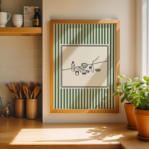 Puede incluir: Una impresi&oacute;n art&iacute;stica enmarcada con un fondo a rayas verdes y blancas. La obra de arte presenta un dibujo lineal negro minimalista de varios art&iacute;culos de cocina, incluyendo botellas, cuencos y utensilios. El marco es de madera clara. Dos plantas en maceta est&aacute;n sobre una superficie de madera.