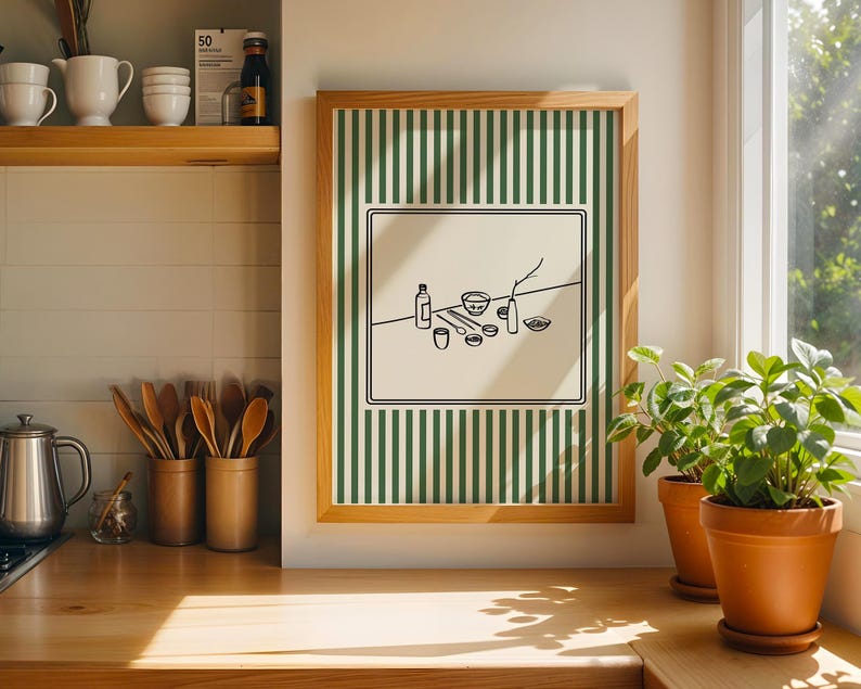 Puede incluir: Una impresi&oacute;n art&iacute;stica enmarcada con un fondo a rayas verdes y blancas. La obra de arte presenta un dibujo lineal negro minimalista de varios art&iacute;culos de cocina, incluyendo botellas, cuencos y utensilios. El marco es de madera clara. Dos plantas en maceta est&aacute;n sobre una superficie de madera.