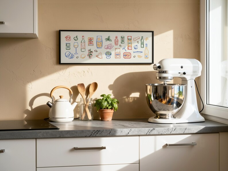 May include: A white stand mixer with a stainless steel bowl sits on a countertop next to a white kettle and a framed print of food illustrations. Wooden spoons and a small potted plant are also on the counter. The kitchen has white cabinets.