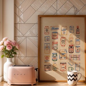 May include: A pink retro-style toaster sits next to a framed print of illustrated grocery items. A white vase with pink roses and a black and white zig-zag patterned mug complete the kitchen scene. The print features various food products.