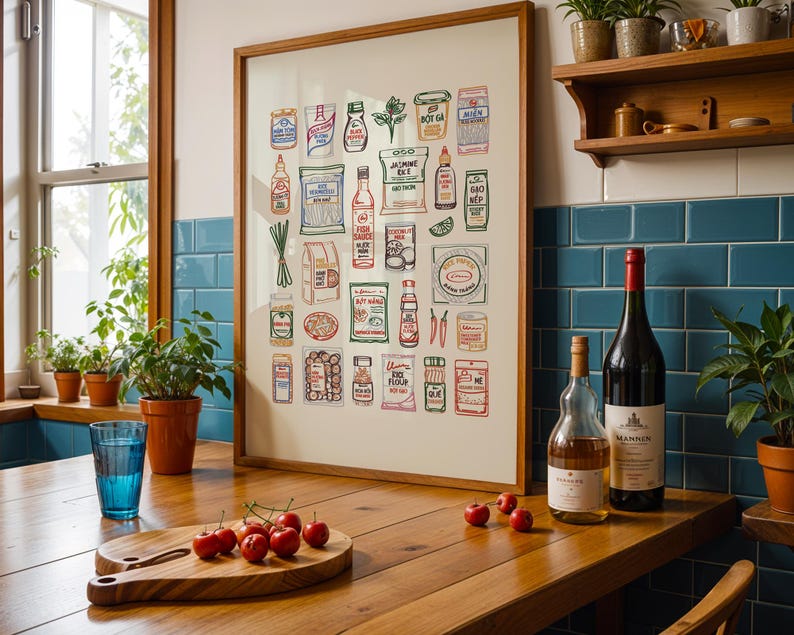 May include: A framed print of illustrated Asian food products hangs above a wooden table. A blue glass, a wooden cutting board with cherries, and two bottles of wine are on the table. Potted plants and a window are in the background.