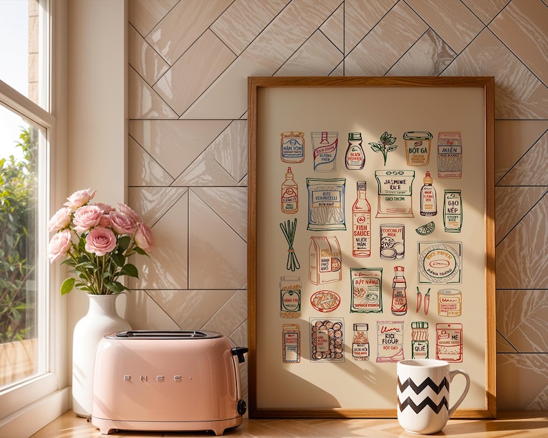 May include: A pink SMEG toaster sits next to a white vase with pink roses and a framed print of Asian food items. A white mug with a black zigzag pattern is in front of the print.