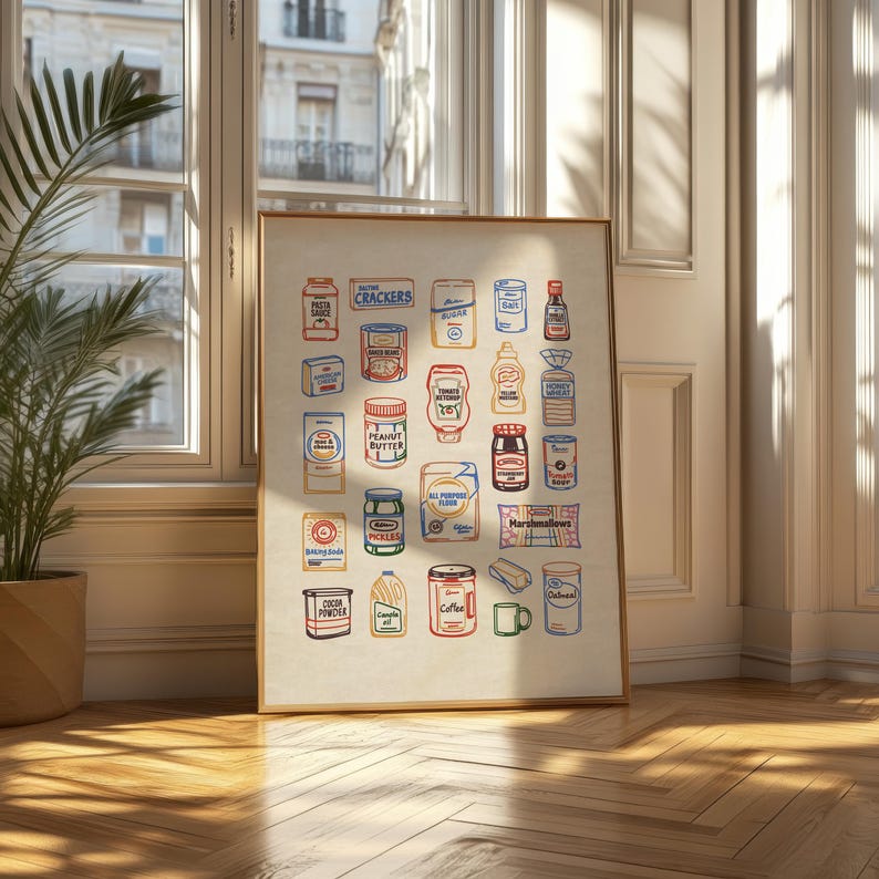 May include: A framed print featuring a colorful illustration of various pantry staples. The artwork includes images of pasta, crackers, peanut butter, and coffee, among other items. The print is displayed in a room with a window and a potted plant.