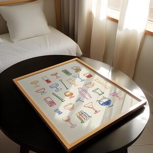 Op de afbeelding: Een ingelijste print met kleurrijke illustraties van verschillende bartools en glaswerk, waaronder cocktailshakers, glazen en roerstaafjes. Het kunstwerk heeft een lichte houten lijst en wordt gepresenteerd op een donkere ronde tafel.