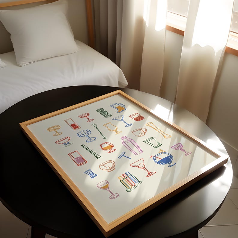 Op de afbeelding: Een ingelijste print met kleurrijke illustraties van verschillende bartools en glaswerk, waaronder cocktailshakers, glazen en roerstaafjes. Het kunstwerk heeft een lichte houten lijst en wordt gepresenteerd op een donkere ronde tafel.