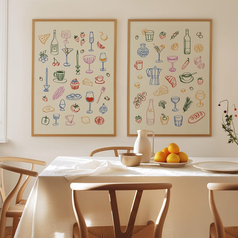 Puede incluir: Dos impresiones enmarcadas con ilustraciones de varios alimentos y bebidas, incluyendo copas de vino, fruta, pan y queso. Las impresiones est&aacute;n colgadas en una pared blanca sobre una mesa con un mantel blanco, dos sillas de madera y un cuenco de naranjas.